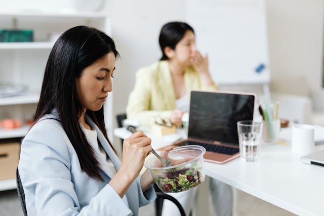 Illustrative image A Woman in a Blue Blazer Eating Salad in the Office used in Accordemy®'s training on Health and Wellness at Work