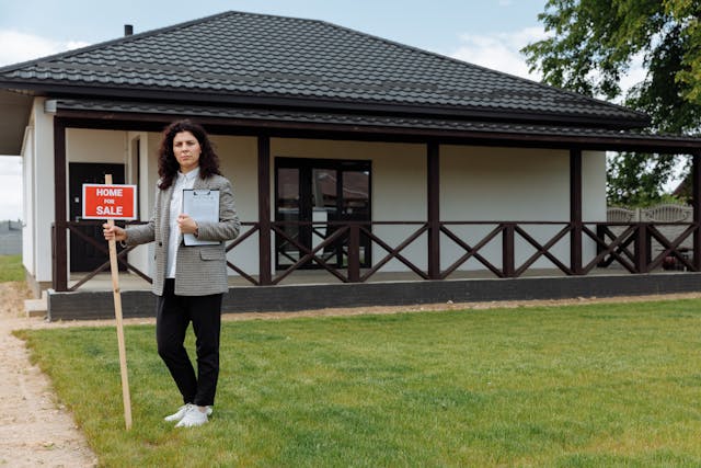 Illustrative image A Woman in Gray Blazer Standing on Green Grass Near the House used in Accordemy®'s training on Managing Multiple Land Affair Projects
