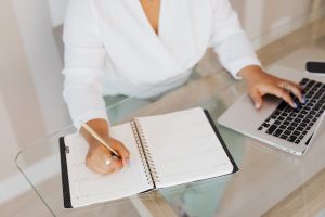 Illustrative image Person Writing on Notebook while Using a Laptop used in Accordemy®'s training on Prioritization and Task Management