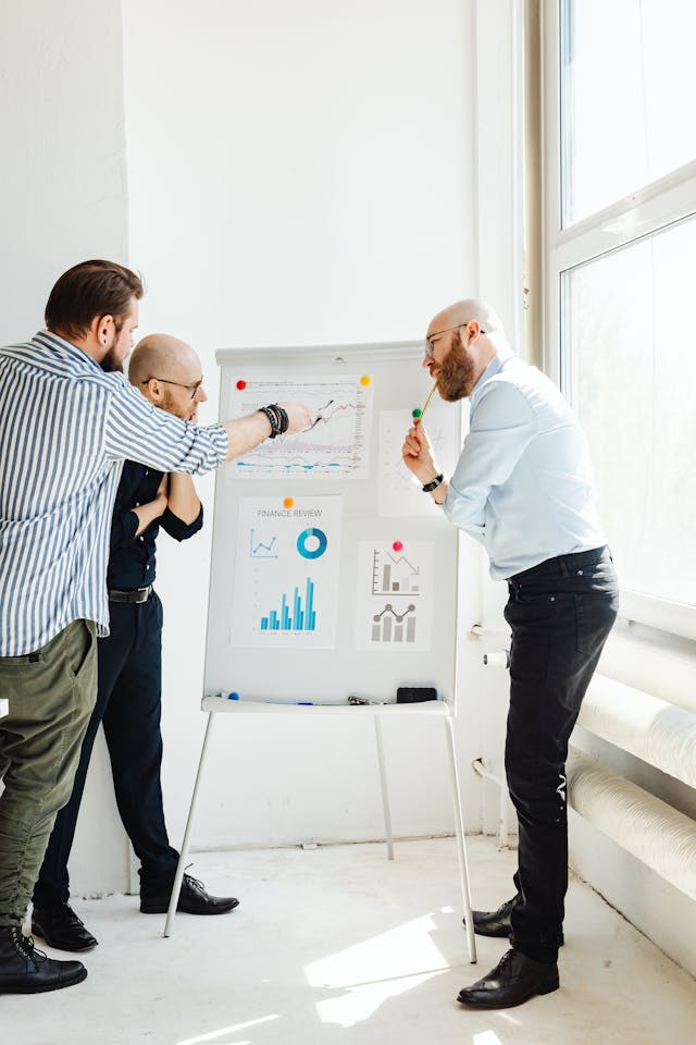 Illustrative image Three Men Discussing Stock Review Charts used in Accordemy®'s training on Writing Winning Proposals for Relief and Development Projects