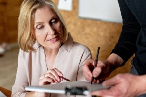 Illustrative image A Woman Looking at a Notebook with a Person Standing Beside Her used in Accordemy®'s training on Collaborative Business Writing