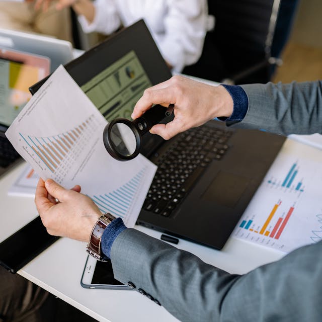 Illustrative image A Person Using a Magnifying Glass on a Document used in Accordemy®'s training on Review of Financial Accounting and Detecting Fraud